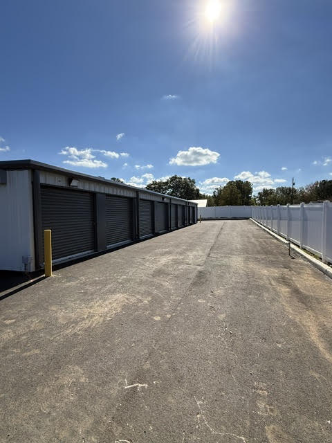 Paved drive between charcoal storage units and a white privacy fence