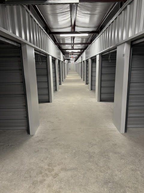 Lit indoor hallway lined with gray roll-up storage unit doors