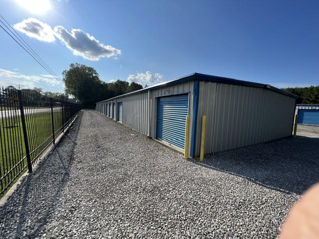 Gravel drive between a storage building and a black iron perimeter fence