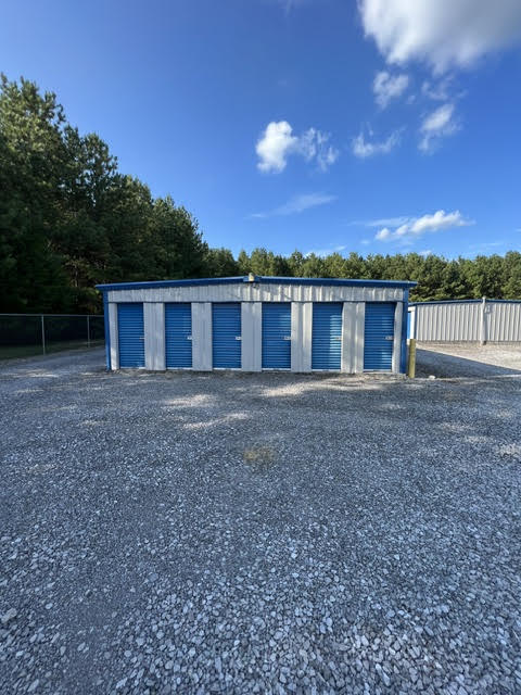 Storage building with six blue roll-up doors in front of tall pine trees