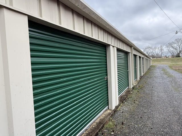 Row of green drive-up storage unit doors along a gravel drive